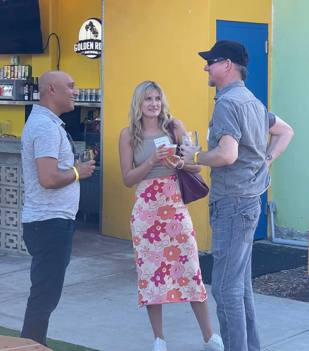 Three people standing and talking among themselves outside near the open bar.